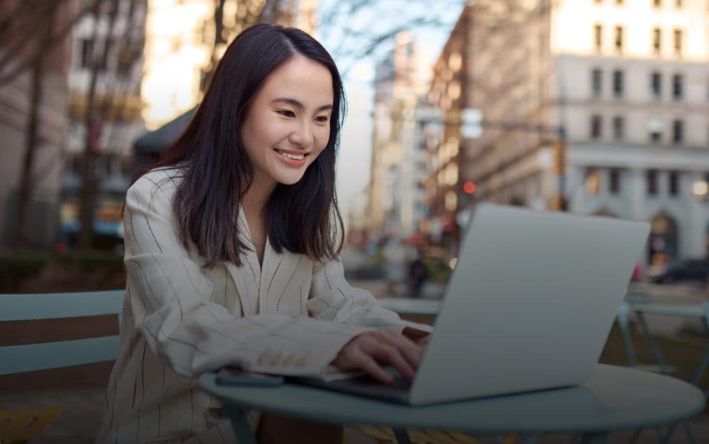 A founder smiling at her laptop at an outdoor café table