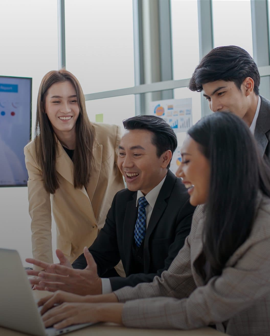 Four young professionals smiling around a laptop in a bright office